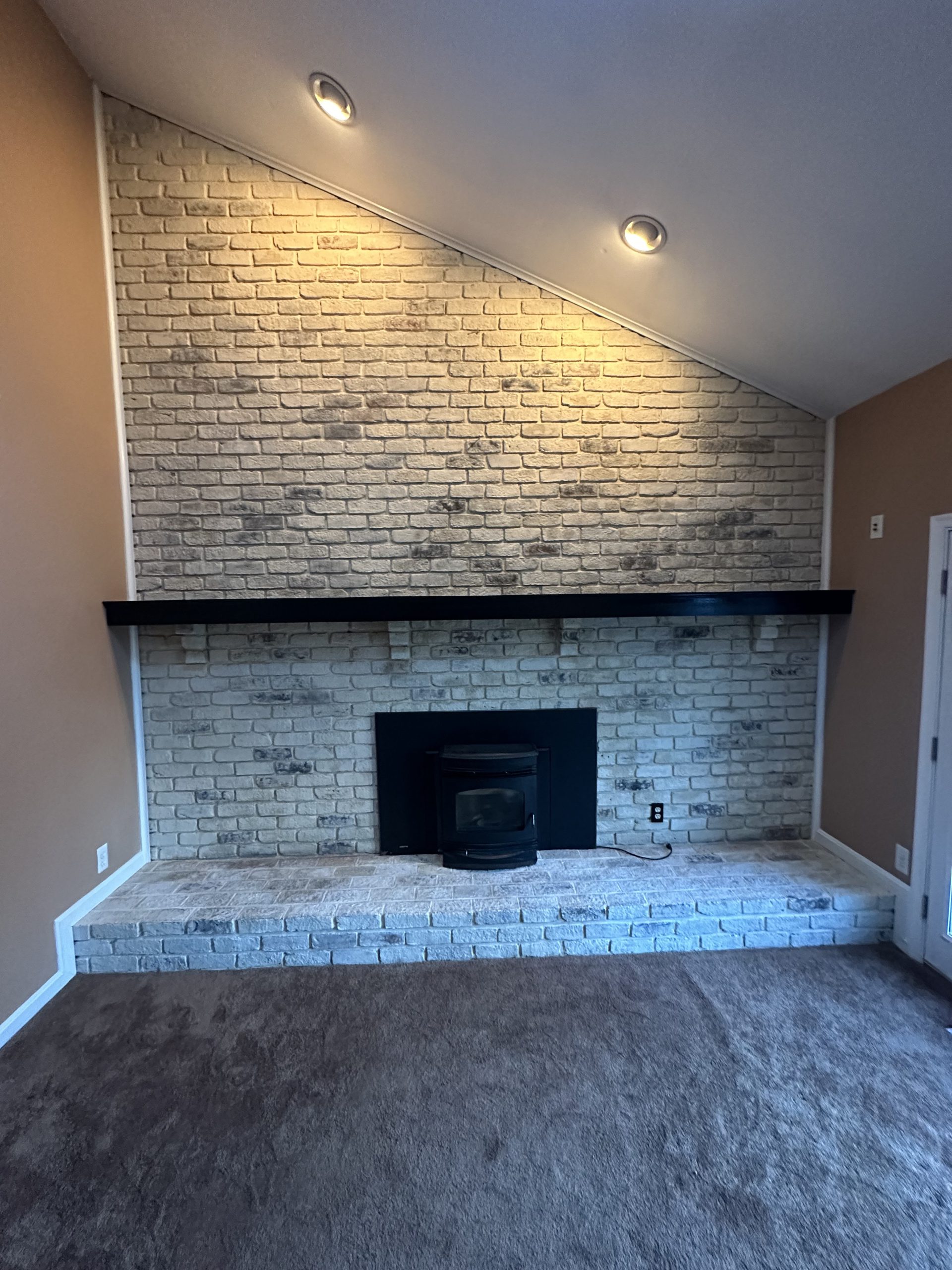 After photo of modern brick fireplace and chimney installation with recessed lighting and dark wood mantel in a residential living room