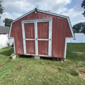 Old red wooden shed with weathered paint and damaged trim before renovation